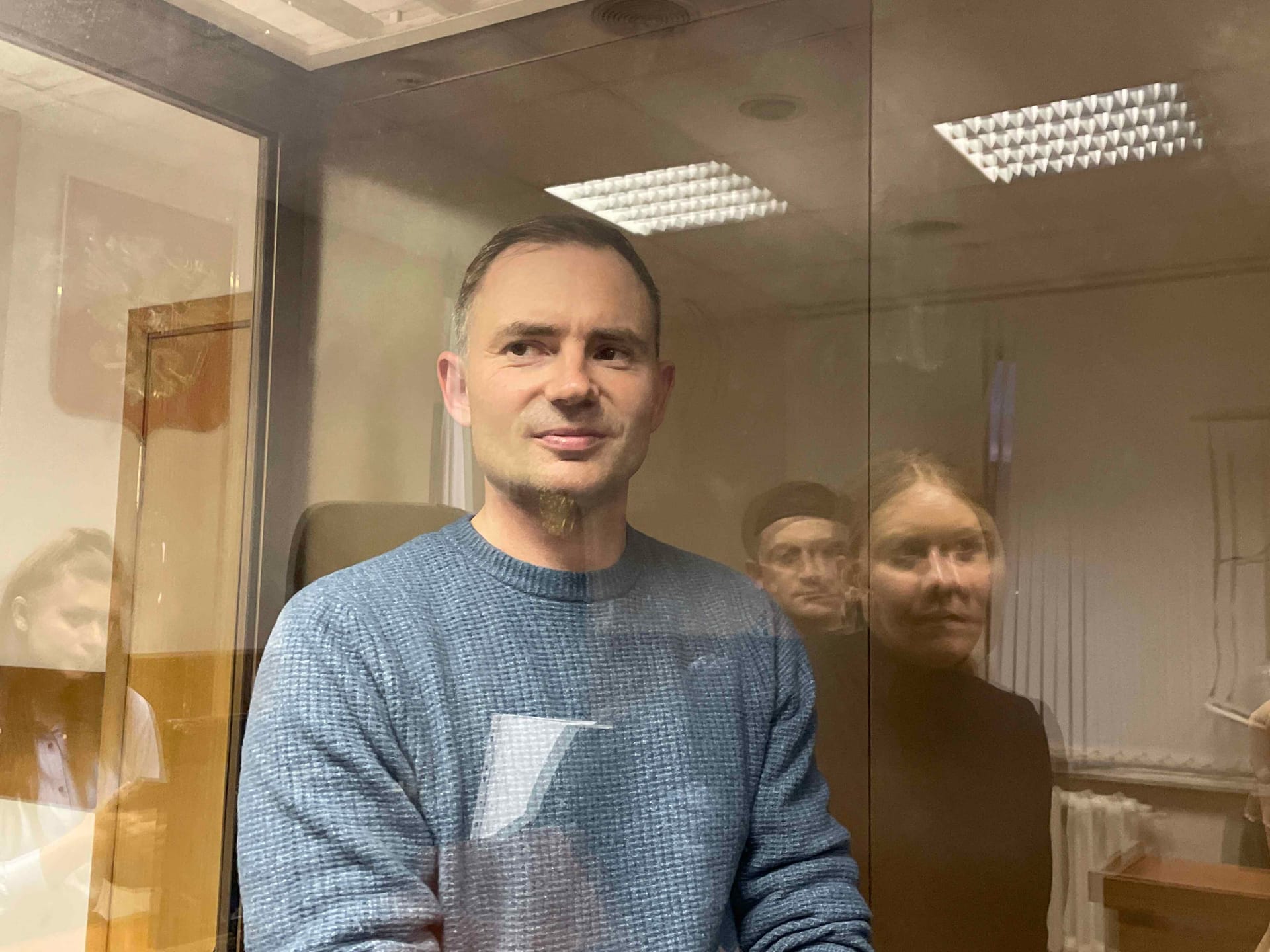 Максим Круглов в судебном аквариуме в ожидании вынесениях ему меры пресечения в виде заключения под стражу. Женщина в черном в отражении – его адвокат Наталия Тихонова. 